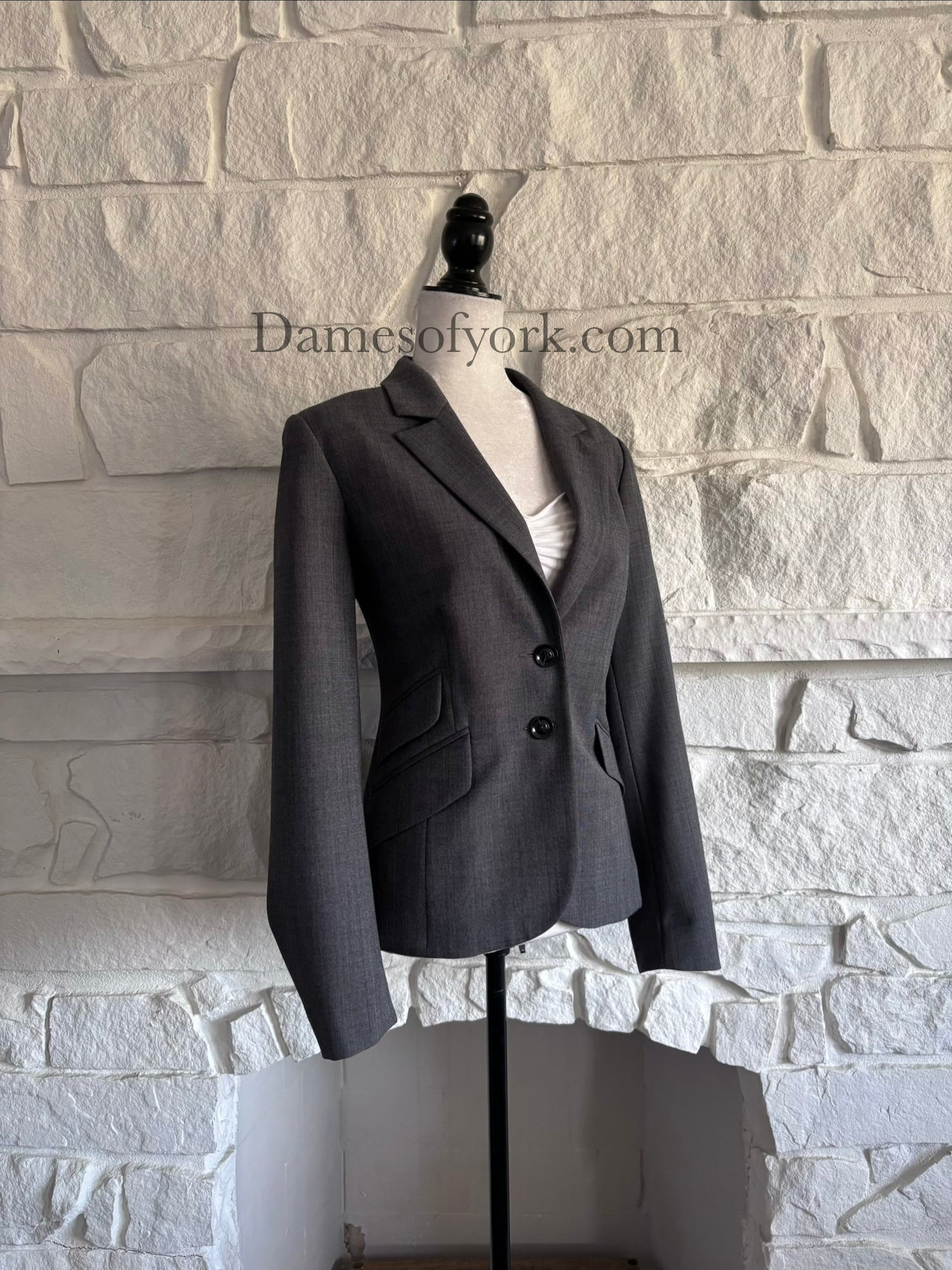 Front view of fitted grey blazer on mannequin with two-button closure and pocket details