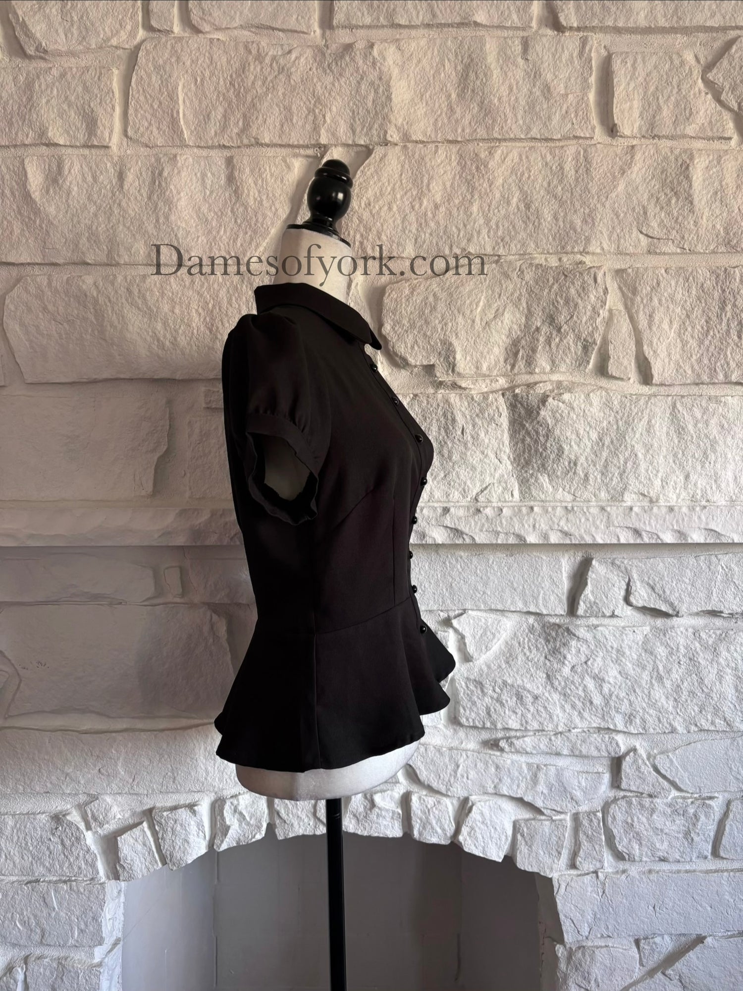 Side view of black vintage-inspired blouse on mannequin with flared peplum silhouette