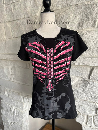A close-up front view of a black gothic graphic t-shirt featuring a pink ribcage shaped like a heart with printed lace-up detail and a subtle grey skeleton design underneath, styled in an emo-inspired alternative design.