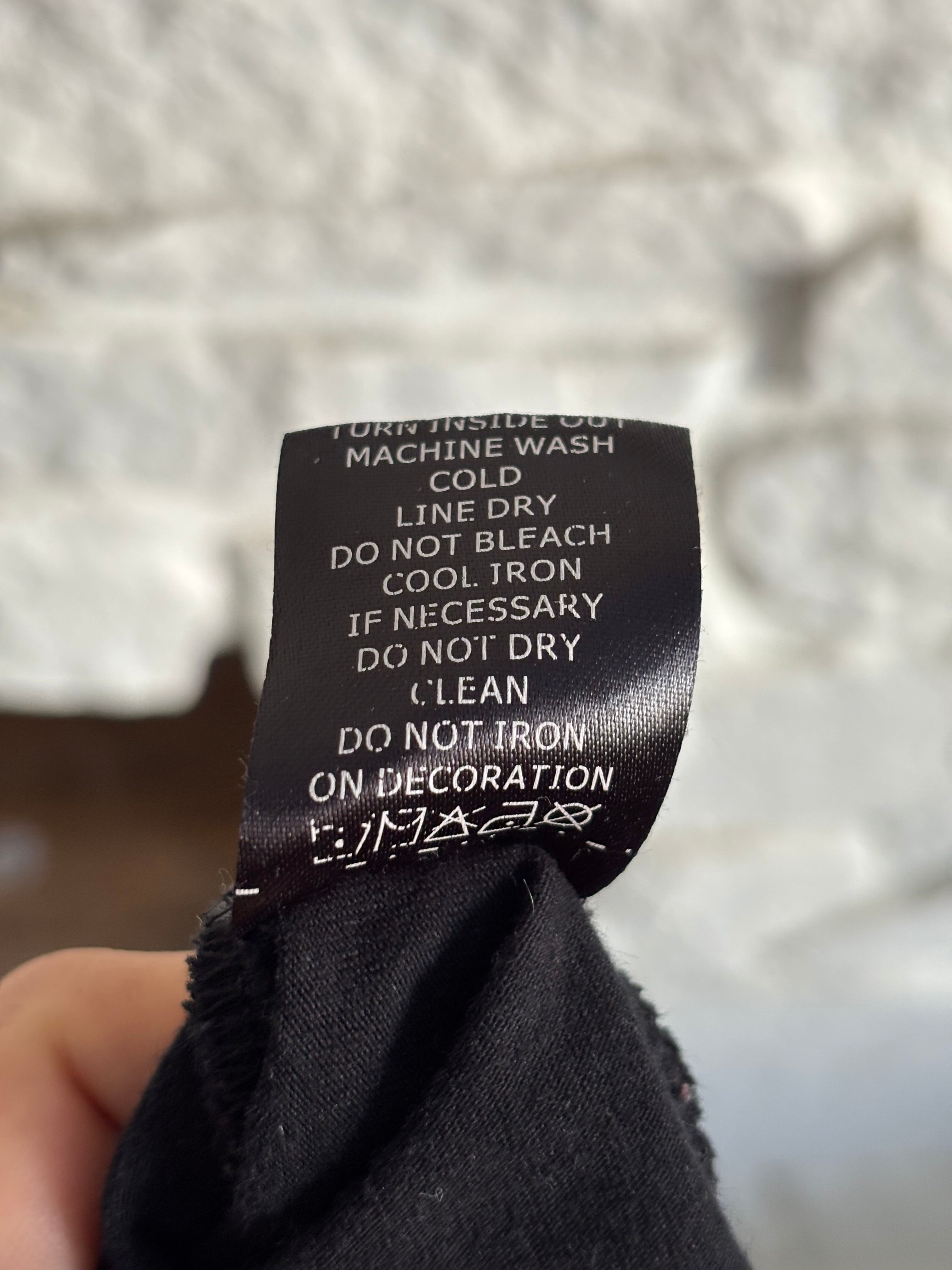 Close up of tag with washing instructions that says "Turn inside out, machine wash cold, line dry, do not bleach, cool iron if necessary, do not dry clean, do not iron on decoration."