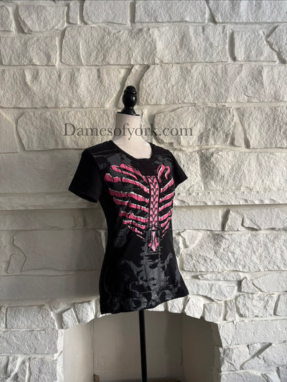 Diagonal view of a black gothic graphic t-shirt featuring a pink ribcage shaped like a heart with printed lace-up detail and a subtle grey skeleton design underneath, styled in an emo-inspired alternative design.