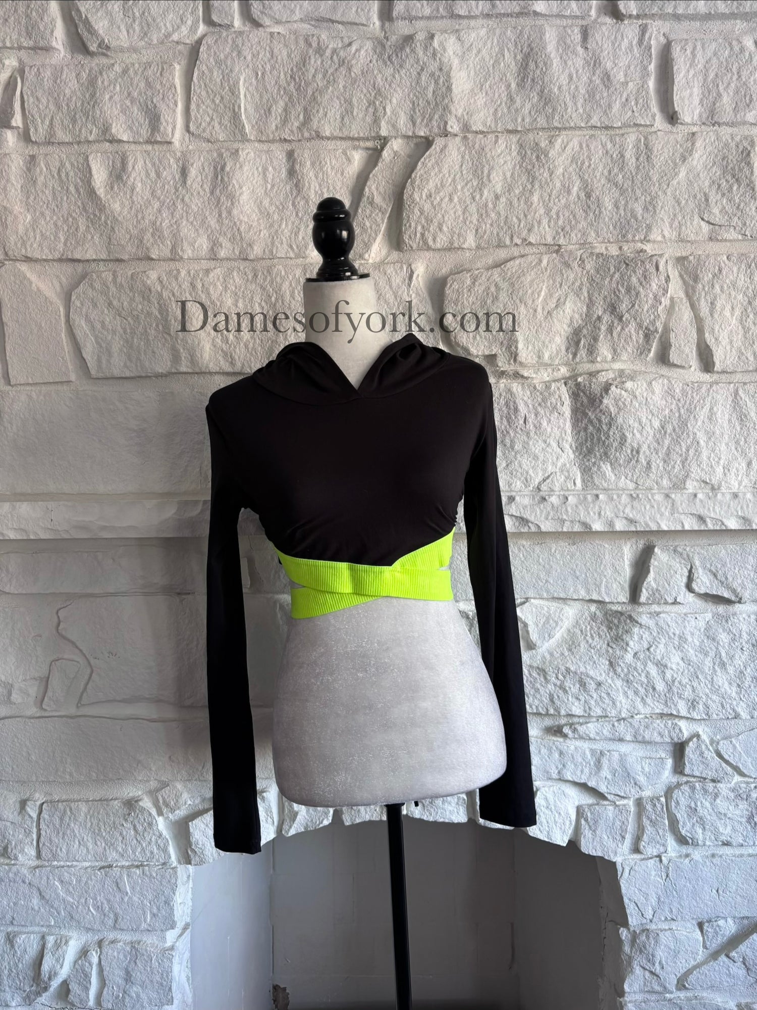Front view of the Neon Circuit Crop Hoodie, a black knit cropped hoodie with neon yellow criss-cross bands creating triangular cutout details on the sides.