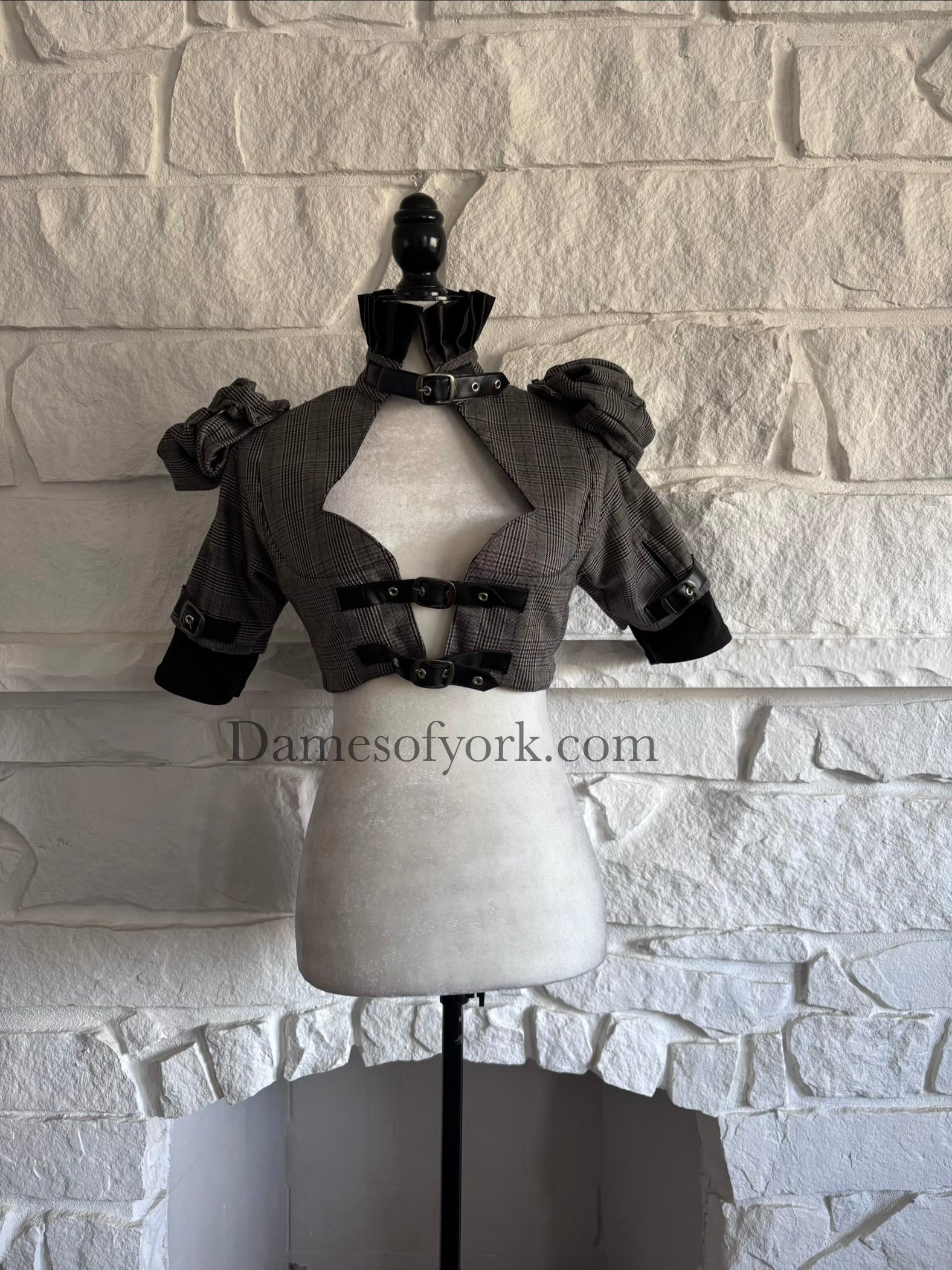 Front view of grey plaid Victorian goth bolero on mannequin with black ruffle collar and buckle details