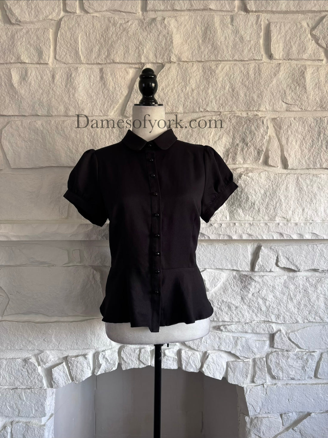 Front view of black peplum button-up blouse on mannequin with Peter Pan collar