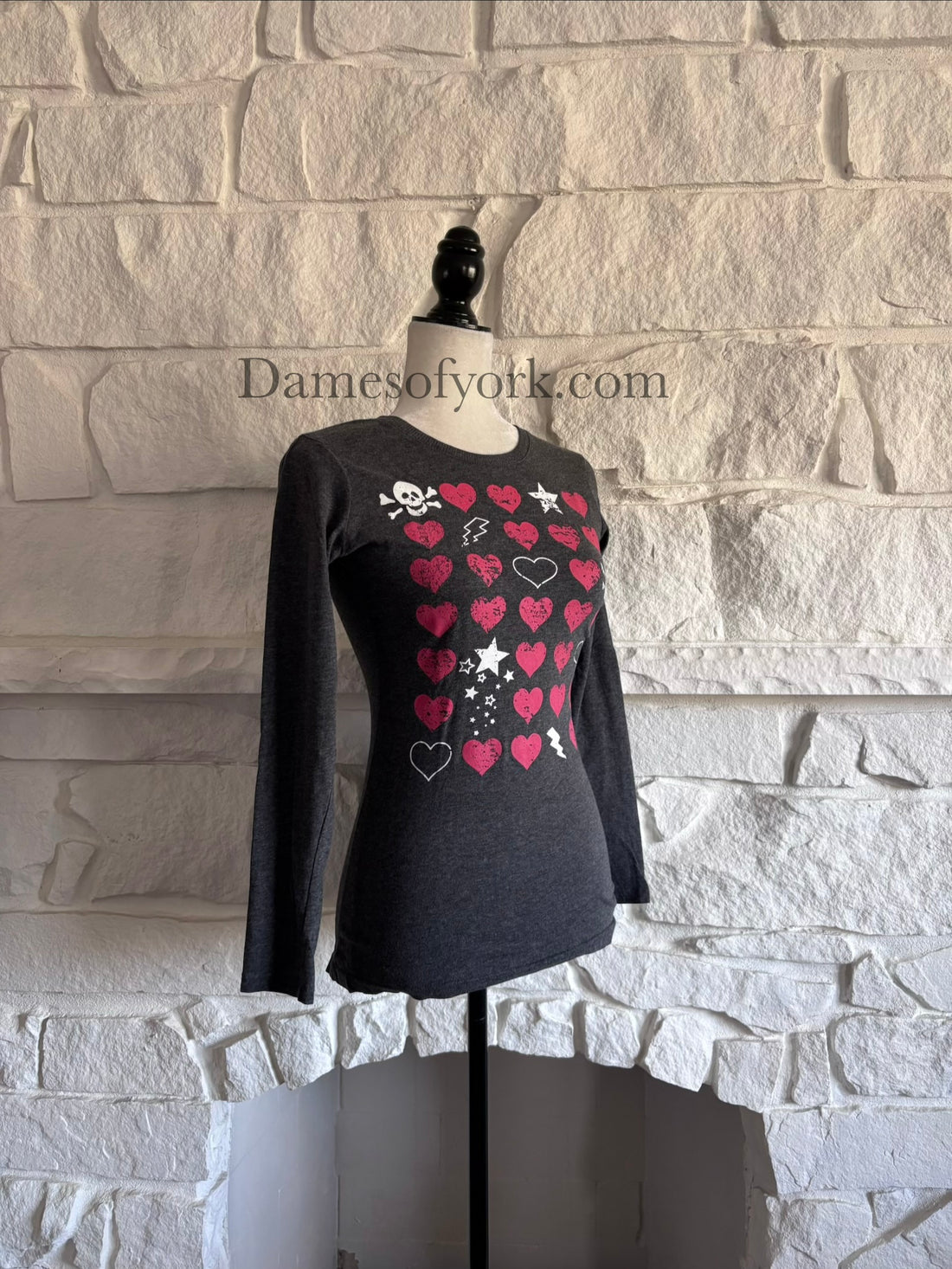 Diagonal view of Y2K style grey long sleeve tee on mannequin showing a skulls, hearts and lightning bolt pattern in a grid configuration 
