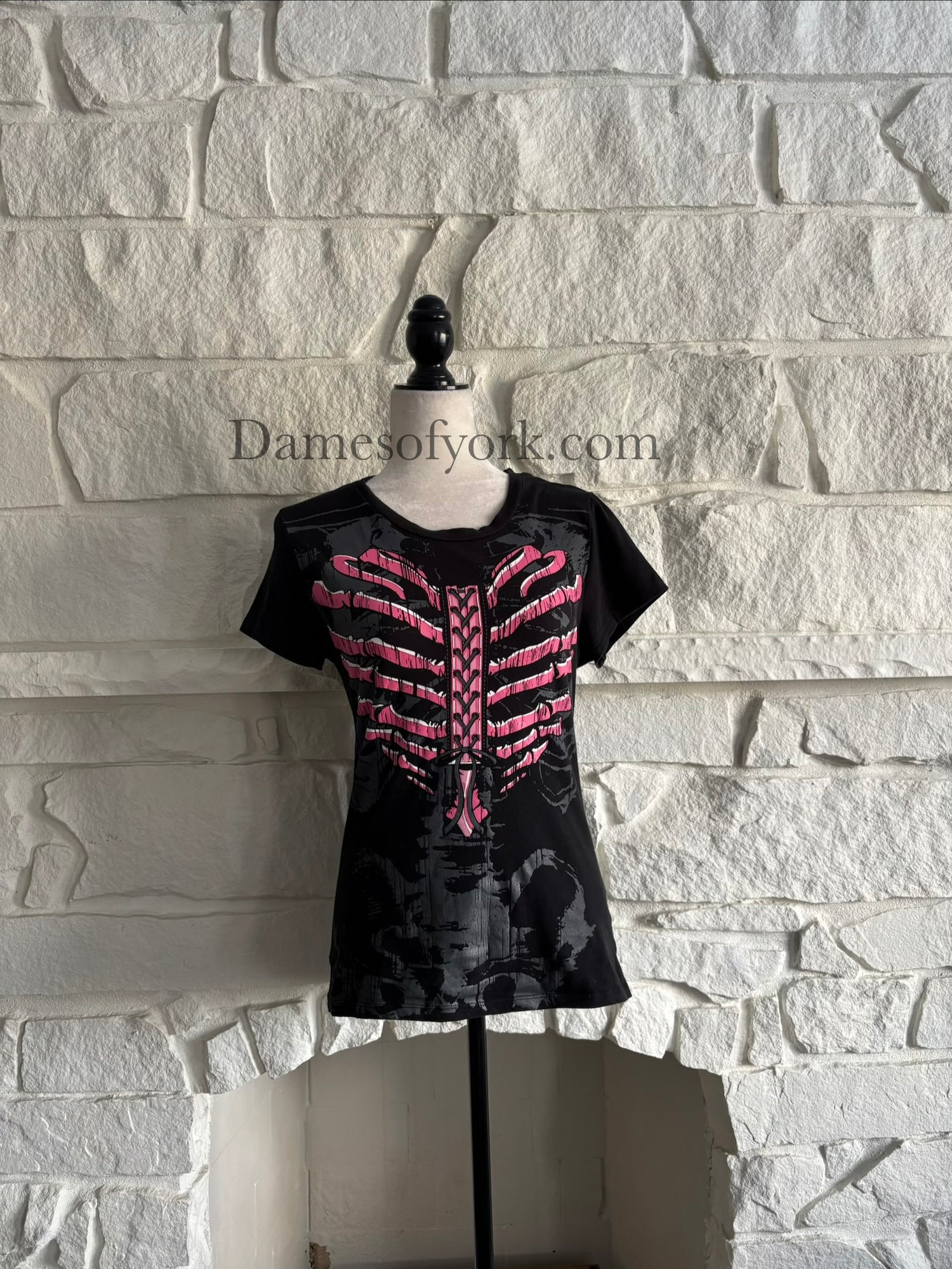 Front view of a black gothic graphic t-shirt featuring a pink ribcage shaped like a heart with printed lace-up detail and a subtle grey skeleton design underneath, styled in an emo-inspired alternative design.